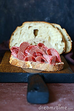 Sliced â€‹â€‹smoked sausage on toast, yeast bread bruschetta on a board on a dark background. Italian, spanish appetizer Stock Photo